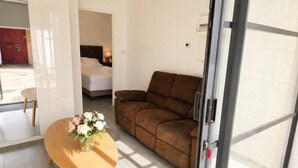Ein Zimmer mit braunem Sofa, einem runden Holztisch mit Blumenvase und einem Bett mit weißer Bettwäsche.