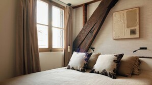 Ein Schlafzimmer mit Bett, einem Fenster mit Vorhängen, einem Holzbalken und einem an der Wand hängenden Kunstwerk.