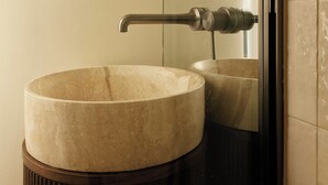 Ein Badezimmer mit einem runden Marmorbecken, einem modernen Wasserhahn und einem spiegelnden Einraumglas.