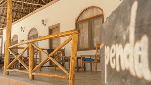 A rustic wooden structure with a bench, a wall-mounted sign, and a window with a wooden frame. - Sunset Mkuu Boutique Hotel (Michamvi)