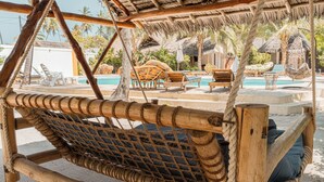 A hammock with a wooden frame and rope netting, a pool area with lounge chairs and umbrellas, and a thatched-roof structure. - Sunset Mkuu Boutique Hotel (Michamvi)