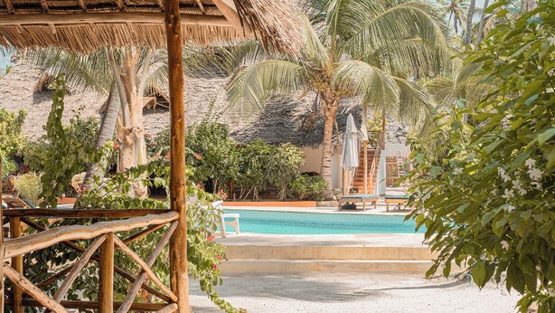 A pool area with a wooden deck, lounge chairs, and palm trees. - Sunset Mkuu Boutique Hotel (Michamvi)
