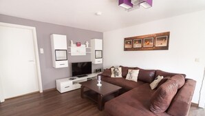 A modern living room with a brown leather sofa, a flat-screen TV, white cabinets, and a wooden coffee table. - NEW! Villa Totti - Anna's parlor (Neßmersiel)