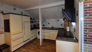 A kitchen with white cabinets, a microwave, a washing machine, and a brick wall. - NEW! Villa Totti - Anna's parlor (Neßmersiel)