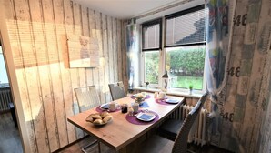 Ein Essbereich mit einem Holztisch, gedeckt für vier Personen, einem Fenster mit Jalousien und einer Heizung.