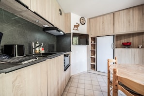 A modern kitchen with wooden cabinets, a black countertop, a built-in oven, and a dining area with a wooden table and chairs. - Mountain View Apartment - Châtel with Balcony, Wi-Fi, and Stunning Scenery (Châtel)