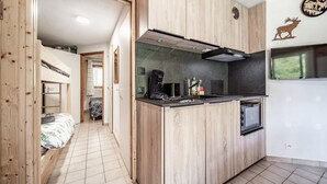 Kompakti keittiö, jossa on puukaapit, sisäänrakennettu mikroaaltouuni ja seinällä oleva kello.