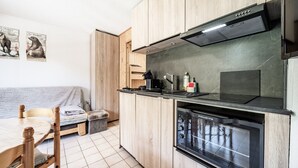 Kompakti keittiö, jossa on puukalusteet, sisäänrakennettu uuni sekä ruokailutila pöytineen ja tuoleineen.