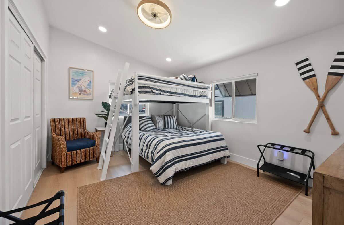 A bunk bed room with a ladder, a chair, a desk, and a wall-mounted paddleboard.