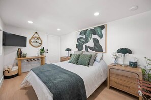 Een slaapkamer met een bed, nachtkastjes, een aan de muur bevestigde televisie en een groot kunstwerk.