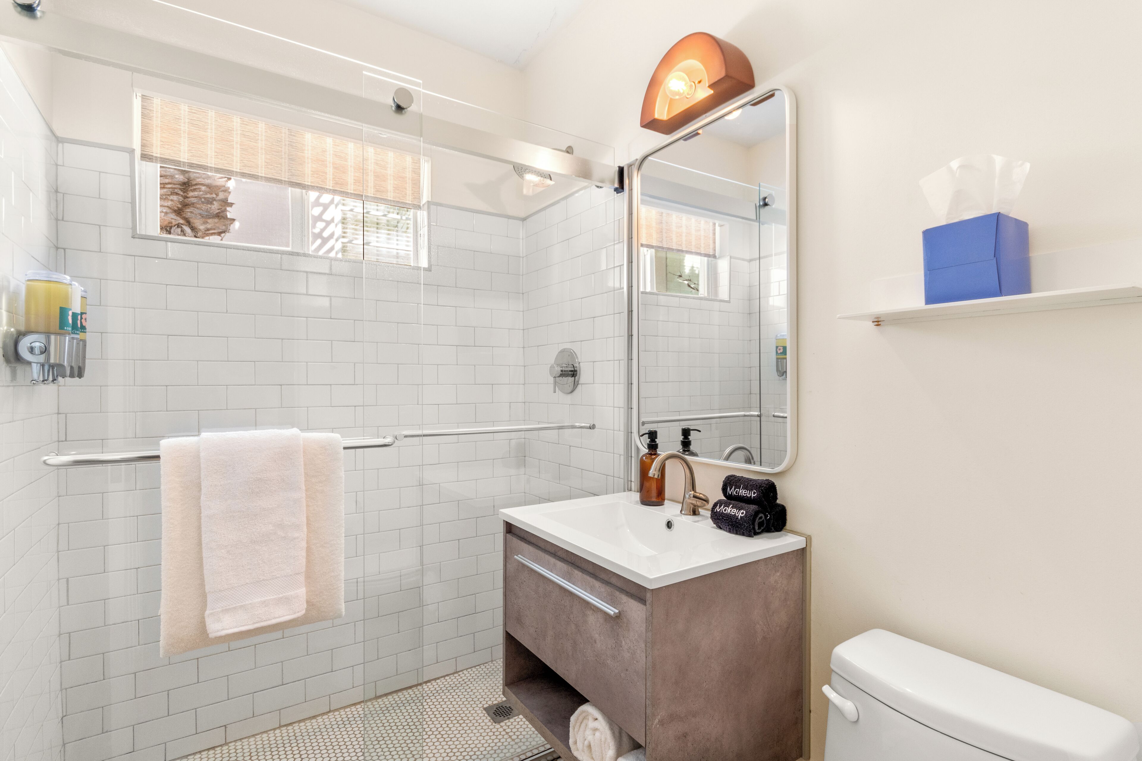 A bathroom with a white tiled shower, a sink with a mirror, a towel rack, and a toilet.