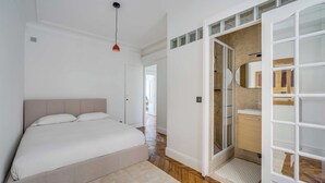 Ein Schlafzimmer mit Bett, einer roten Pendelleuchte, einem begehbaren Kleiderschrank und einem Badezimmer mit Spiegel und Waschbecken.