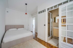 Un dormitorio con cama, una lámpara colgante roja, un vestidor y un baño con espejo y lavamanos.