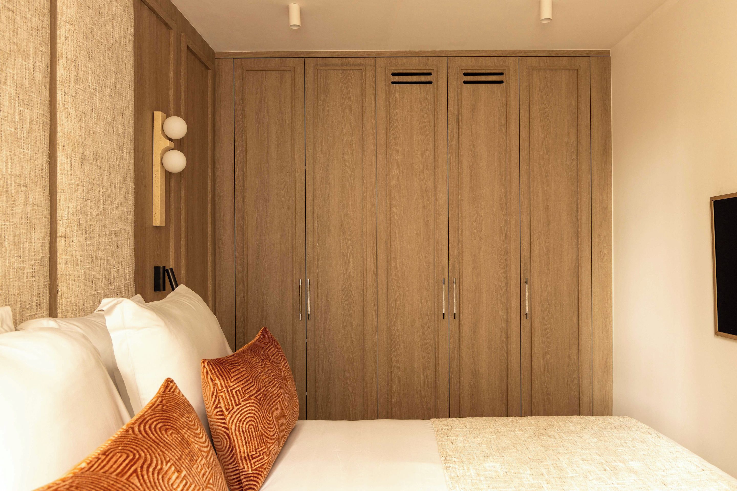 A bedroom with a bed, pillows, a wardrobe, and a wall-mounted TV.