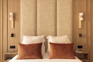 A hotel room with a bed, two patterned pillows, a nightstand with a lamp, and a wall-mounted light fixture. - Refined Apartment a/c 1br/2p - Saint-germain (Paris)