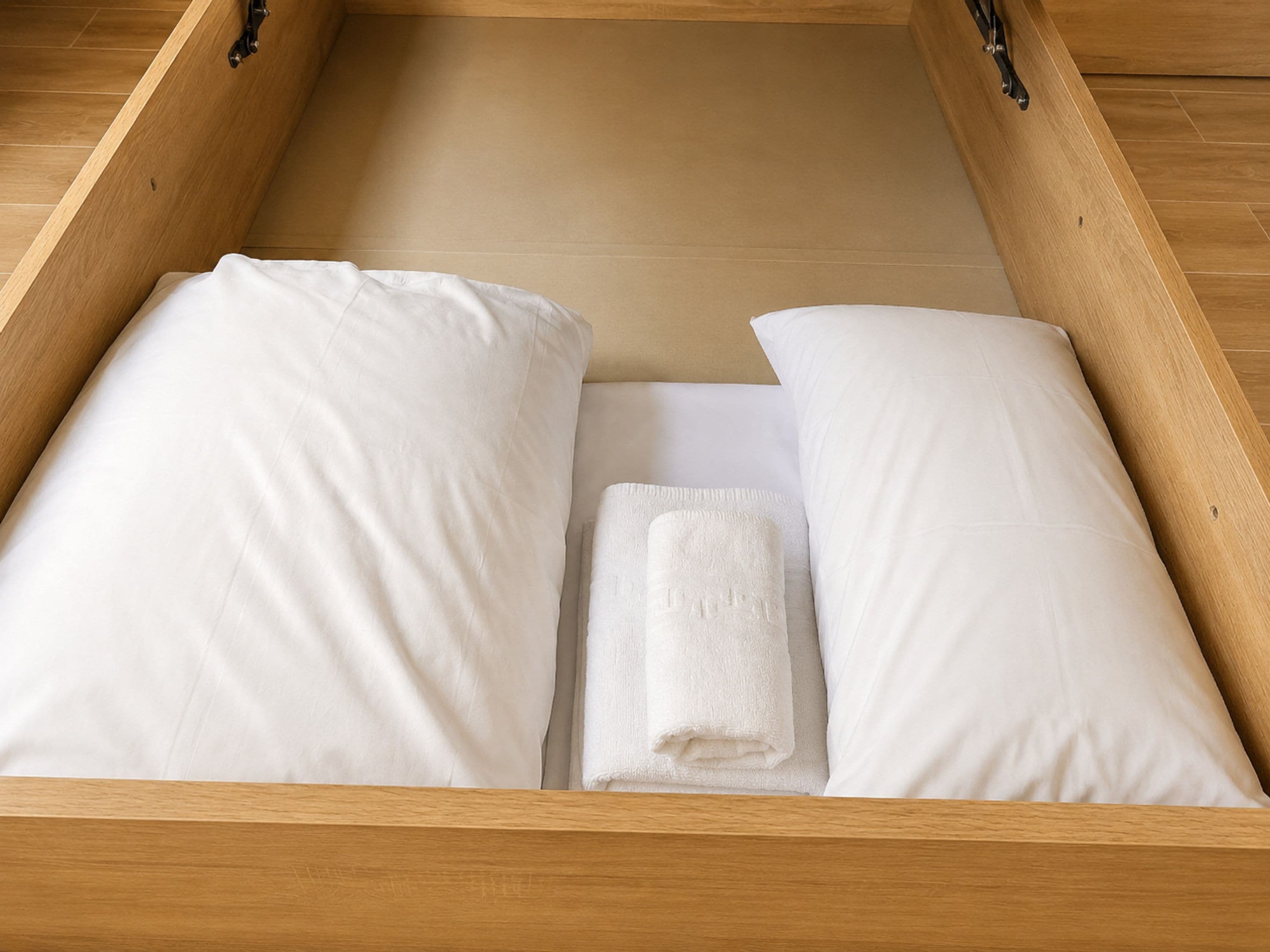 Un armazón de cama de madera con ropa de cama blanca y una toalla doblada.