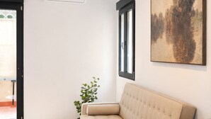 Una sala de estar moderna con un sofá, una mesa de comedor con sillas, un jarrón con flores y un cuadro en la pared.