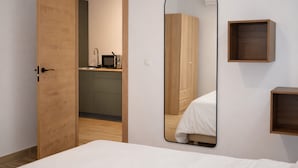 Un dormitorio con una cama, un armario de madera, un espejo y un pequeño estante de madera.