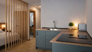 A compact hotel room with a kitchenette, a bed, a wooden partition, and a small potted plant. - Apartment Near the Las Ventas F Bullring (Madrid)