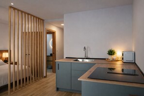 Una habitación de hotel compacta con kitchenette, una cama, un separador de madera y una pequeña planta en maceta.