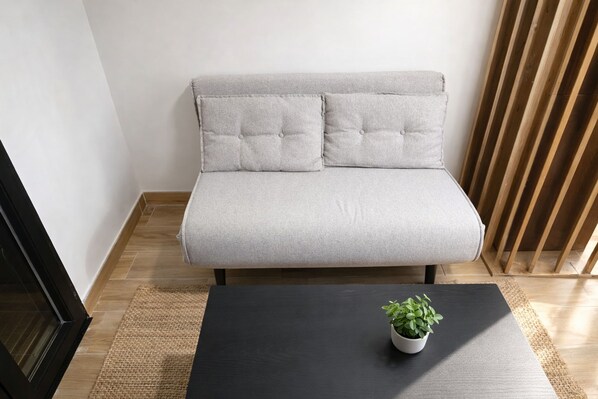 Ein Sofa mit Kissen, ein kleiner Tisch mit Pflanze und Holzboden.