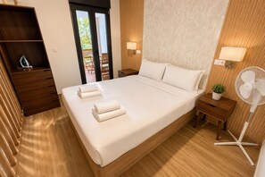 A neatly made bed with white linens, a wooden nightstand with a lamp, a small potted plant, and a standing fan. - Apartment Near the Las Ventas F Bullring (Madrid)
