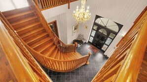 Eine Wendeltreppe mit Holzwertungen und einem Kronleuchter, die zu einem Raum mit Kamin und Außenblick führt.