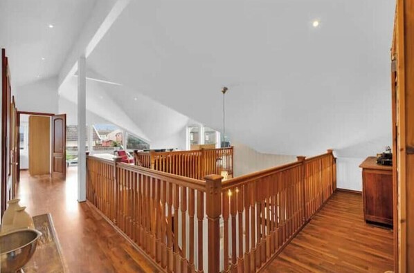 A spacious loft with a high ceiling, wooden railing, and a view of the cityscape.