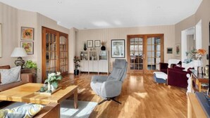 A spacious living room with a wooden floor, a grey armchair, a sofa, and a cabinet with glass doors. - Spacious villa with private pool, 5 bedrooms and 5 bathrooms (Rogaland)