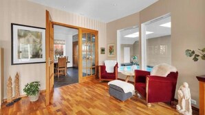 A spacious living area with a wooden floor, red armchairs, a grey ottoman, and a dining area visible through a glass door. - Spacious villa with private pool, 5 bedrooms and 5 bathrooms (Rogaland)