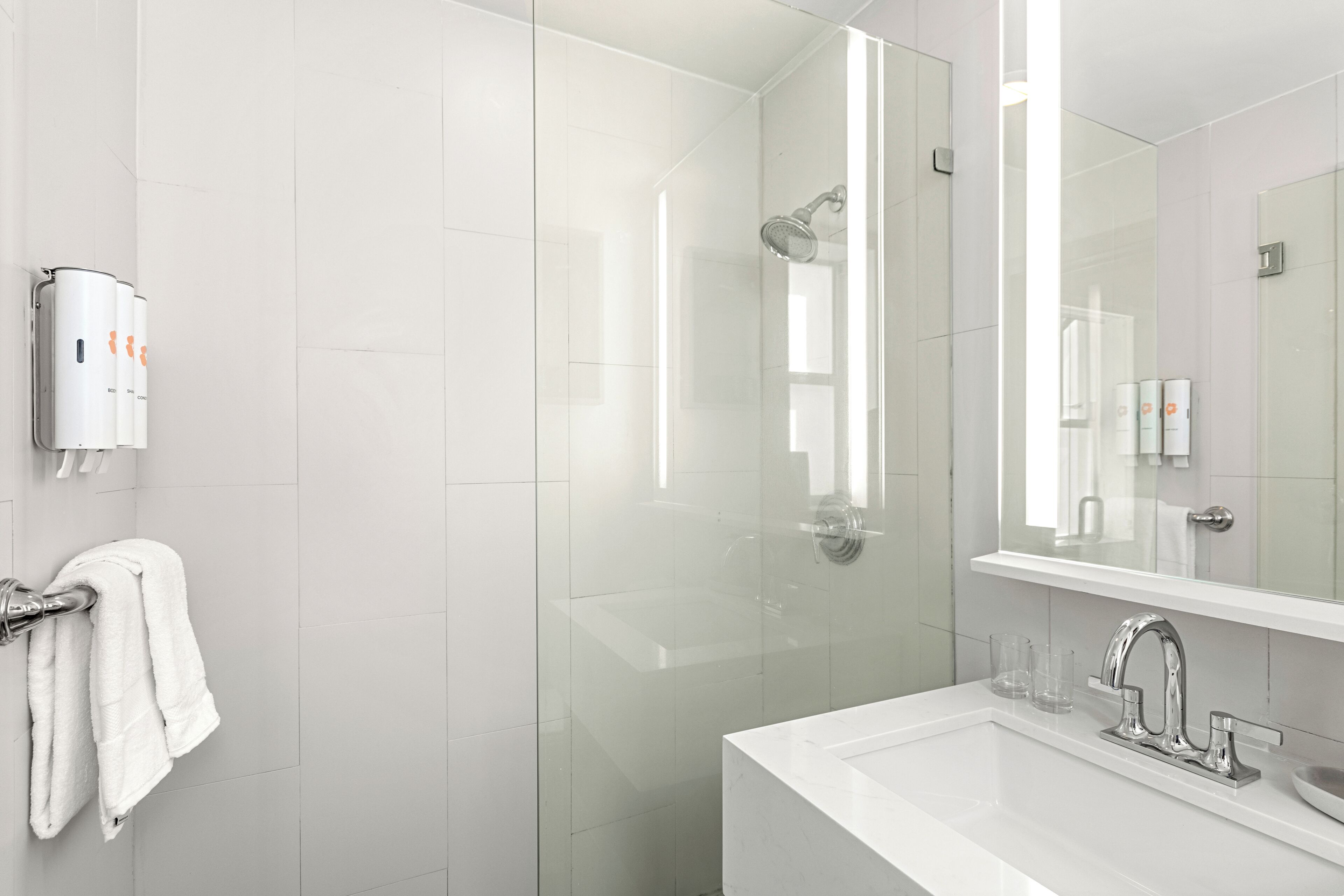 A modern bathroom with a glass-enclosed shower, a white sink with a chrome faucet, and a towel rack with white towels.