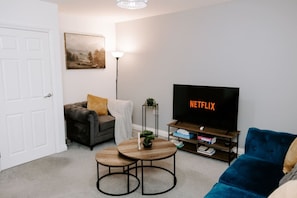 Ein Wohnzimmer mit einer Couch, einem Couchtisch, einem Fernseher und einem Bücherregal.