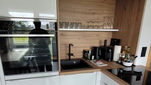 Eine moderne Küche mit weißen Schränken, einem Holzregal, einer schwarzen Spüle und einer Arbeitsplatte mit verschiedenen Gegenständen.