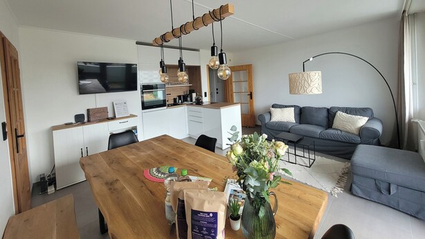 Ein moderner Wohnbereich mit einem Holzesstisch, einer Couch, einem Fernseher und einer Küchenzeile.