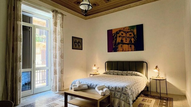A bedroom with a bed, a nightstand, a hanging light fixture, a painting, and a patterned floor. - Le Suite Vintage Del Corso (Palermo)