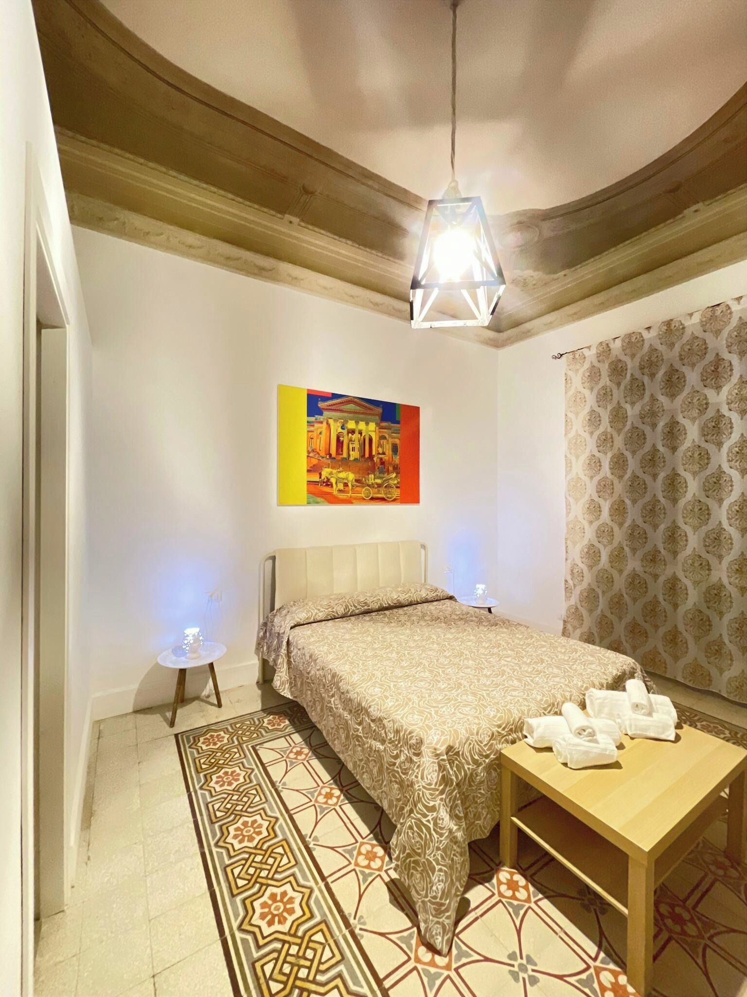 Une chambre à coucher comprenant un lit, une petite table, un luminaire suspendu, un tapis à motifs et un élément décoratif mural.