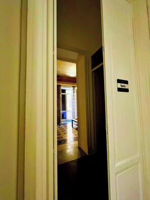 A hallway with a sign reading 'Ninfa' on a door, leading to a room with a patterned floor and a bench. - Le Suite Vintage Del Corso (Palermo)
