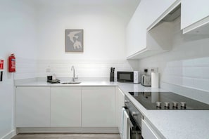 A modern kitchen with white cabinetry, a stainless steel sink, a microwave, a toaster, and a black induction cooktop. - Spacious & Modern 1BED Apartment nr Etihad Stadium (Manchester)