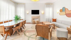 A modern living room with a large glass-top dining table, sofas, a flat-screen TV, and a fireplace.