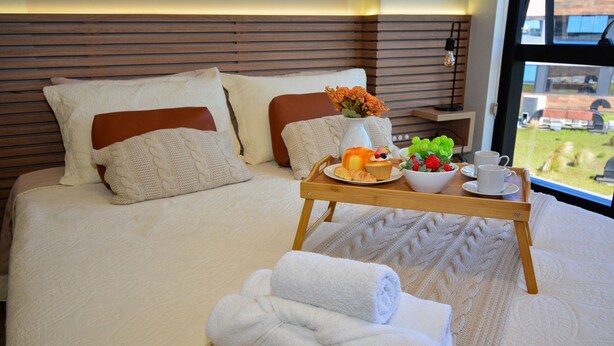 A neatly made bed with a tray of breakfast items, including croissants, fruit, and a cup, in a modern hotel room with a view. - Studio Shopping OKA Floripa - SOK211 (Florianópolis)