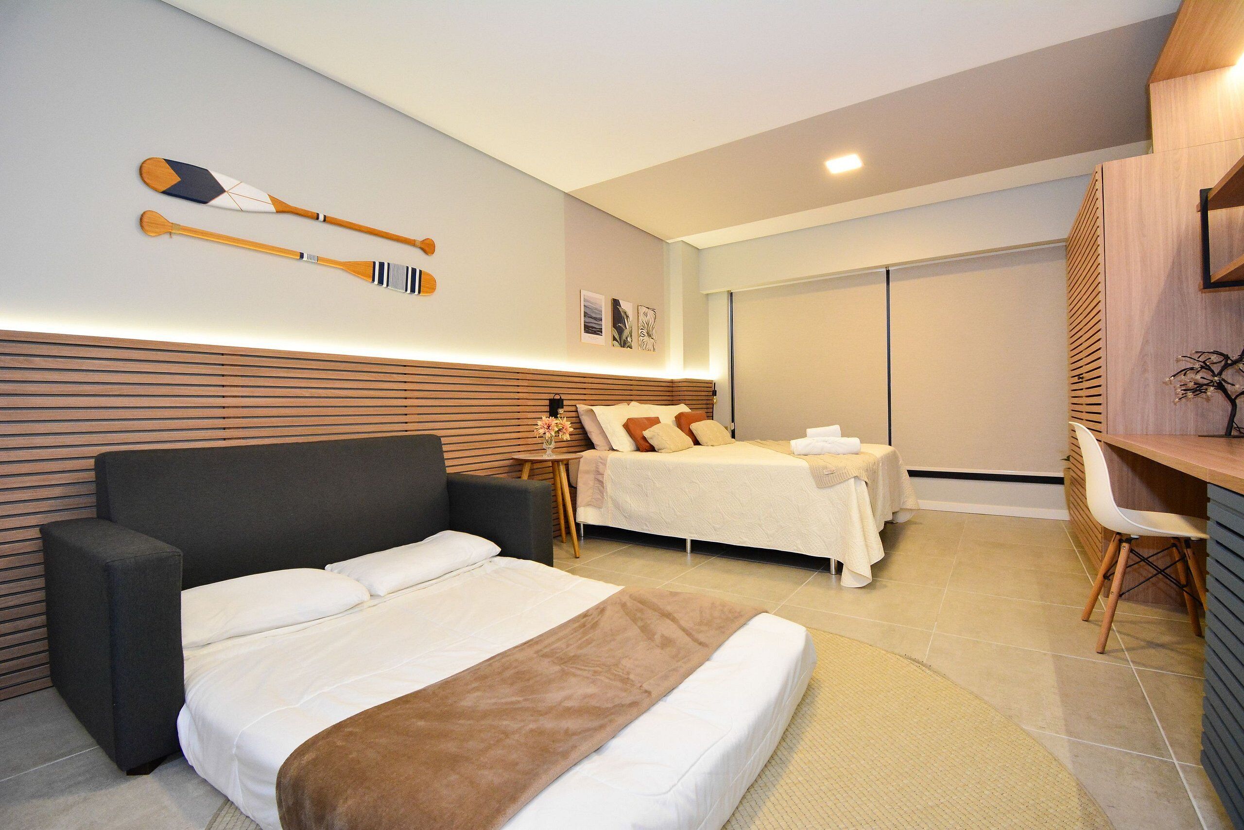 A modern hotel room with a large bed, a smaller bed, a desk, and a chair.
