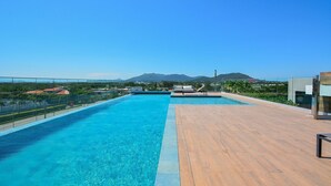 A rooftop swimming pool with clear blue water, wooden deck, and a view of distant mountains. - Studio Shopping OKA Floripa - SOK211 (Florianópolis)