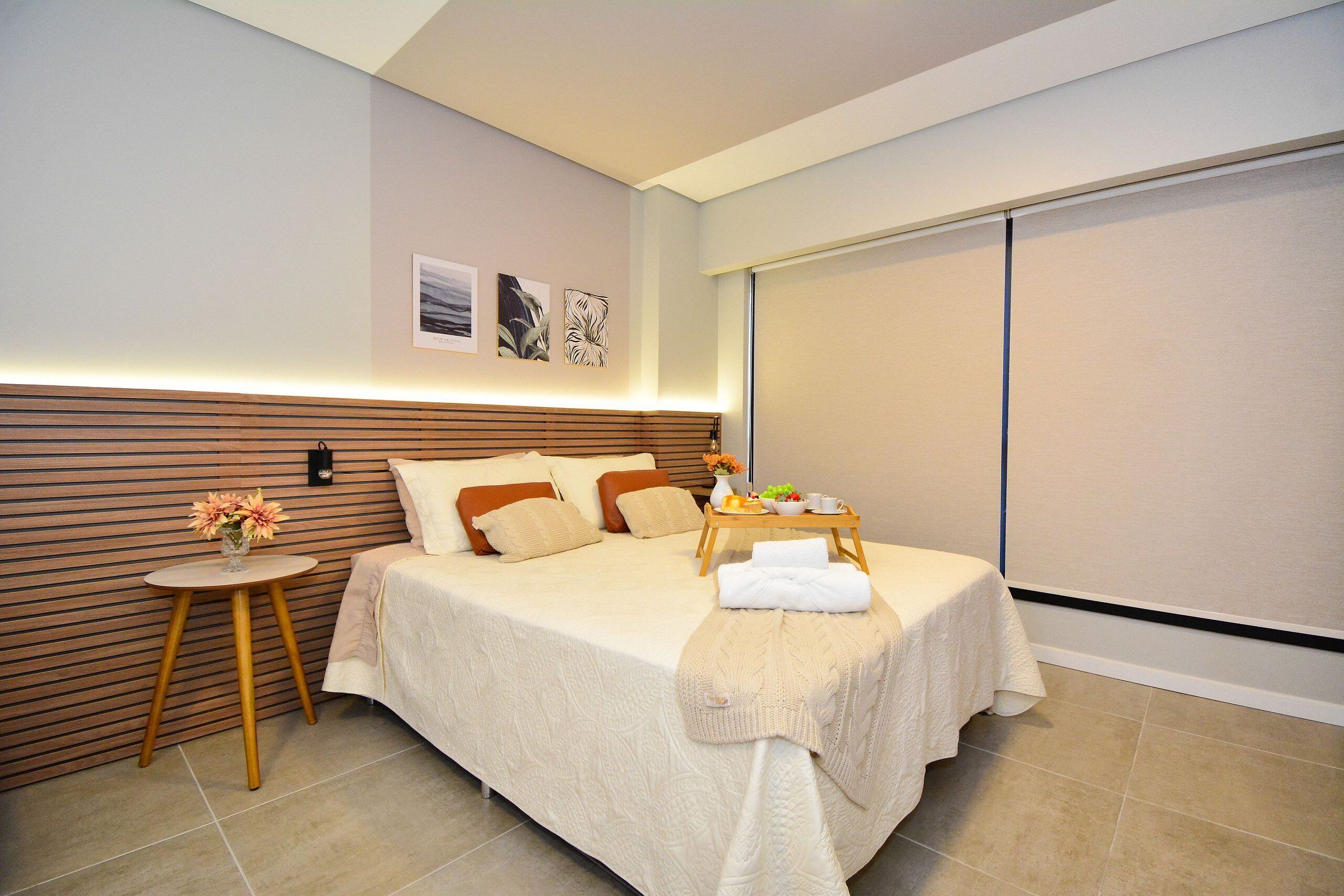 A modern hotel room with a bed, a small round table with a tray, and a wall-mounted shelf.