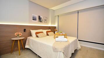 A modern hotel room with a bed, a small round table with a tray, and a wall-mounted shelf.
