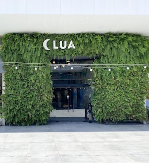 Entrada de un edificio con un arco cubierto de follaje verde y el nombre 'CLUA' encima.