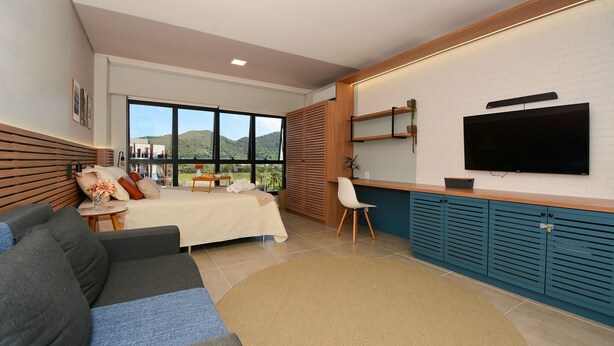 Habitación de hotel moderna con cama, sofá, televisión y vistas al exterior.