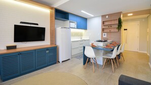A modern kitchen with a flat-screen TV, a refrigerator, and a dining area with chairs and a table. - Studio Shopping OKA Floripa - SOK211 (Florianópolis)