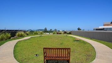 A bench in a landscaped area with a curved pathway, a grassy lawn, and a view of distant hills.