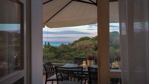 Una terrazza esterna con tavolo e sedie, vista sul mare e un paesaggio collinare.