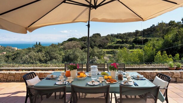 Una tavola apparecchiata per la colazione con vista sul mare e sulle colline.